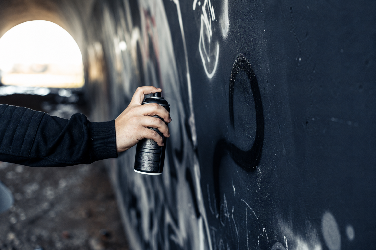 Sprayer besprüht eine Wand mit schwarzer Sprühdose